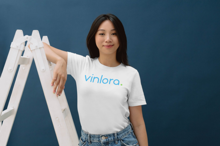 Junge Frau im vinlora-T-Shirt lehnt an einer Leiter und blickt selbstbewusst in die Kamera. Symbolisiert das Engagement und die Identität von vinlora.